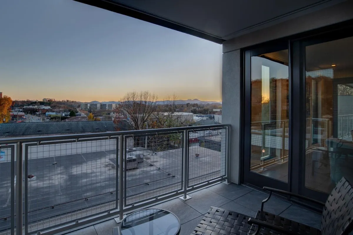 A tranquil exterior view from a private balcony showcases comfortable outdoor furniture, a sturdy railing, and an expansive panorama of the city with mountains rising in the background. The scene is set for either a peaceful morning coffee or an evening watching the sunset, reinforcing the luxury of private outdoor space.