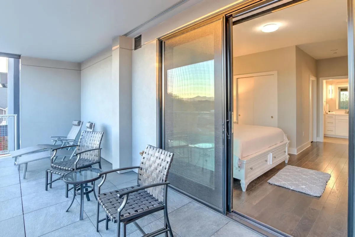 An exterior shot of a patio featuring comfortable chairs, a glass sliding door leading inside, and a glimpse of the bedroom interior. The outdoor table invites relaxation, while the sliding door illustrates seamless access between private indoor and outdoor spaces.