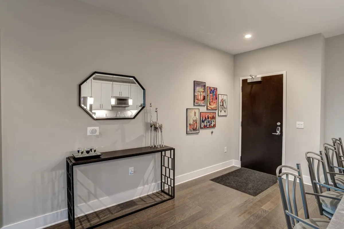 A welcoming entryway featuring a console table topped with a decorative piece, a stylish mirror reflecting the space, and a door suggesting immediate access to the condo. The area is tastefully arranged, providing a sense of arrival and first impressions for guests stepping inside.
