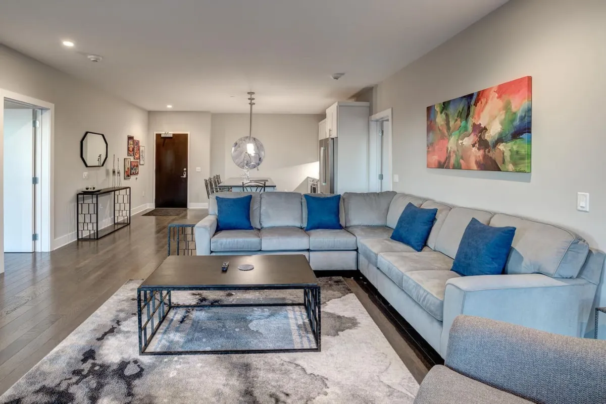 A comfortable living area with a sectional sofa, coffee table, and colorful artwork adorning the wall. The space is well-lit and inviting, ideal for relaxing with friends or unwinding after an active evening.